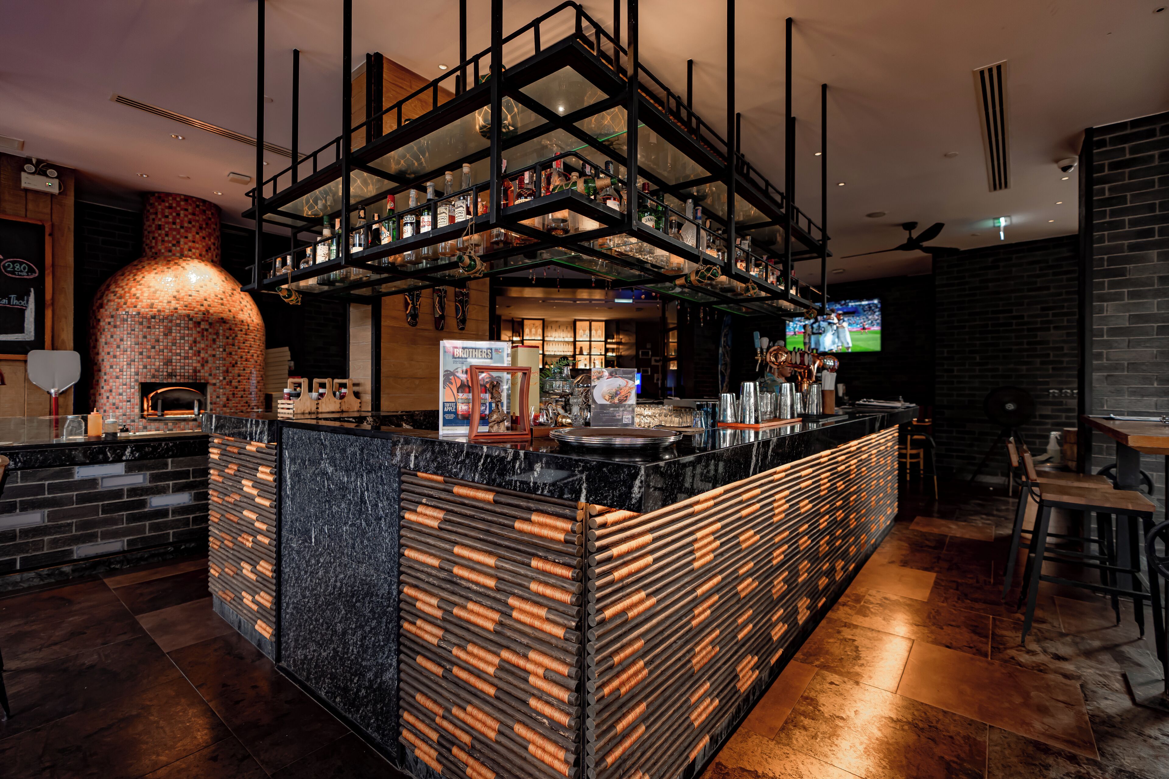 A bar area with a brick wall, a large oven, and a TV screen.