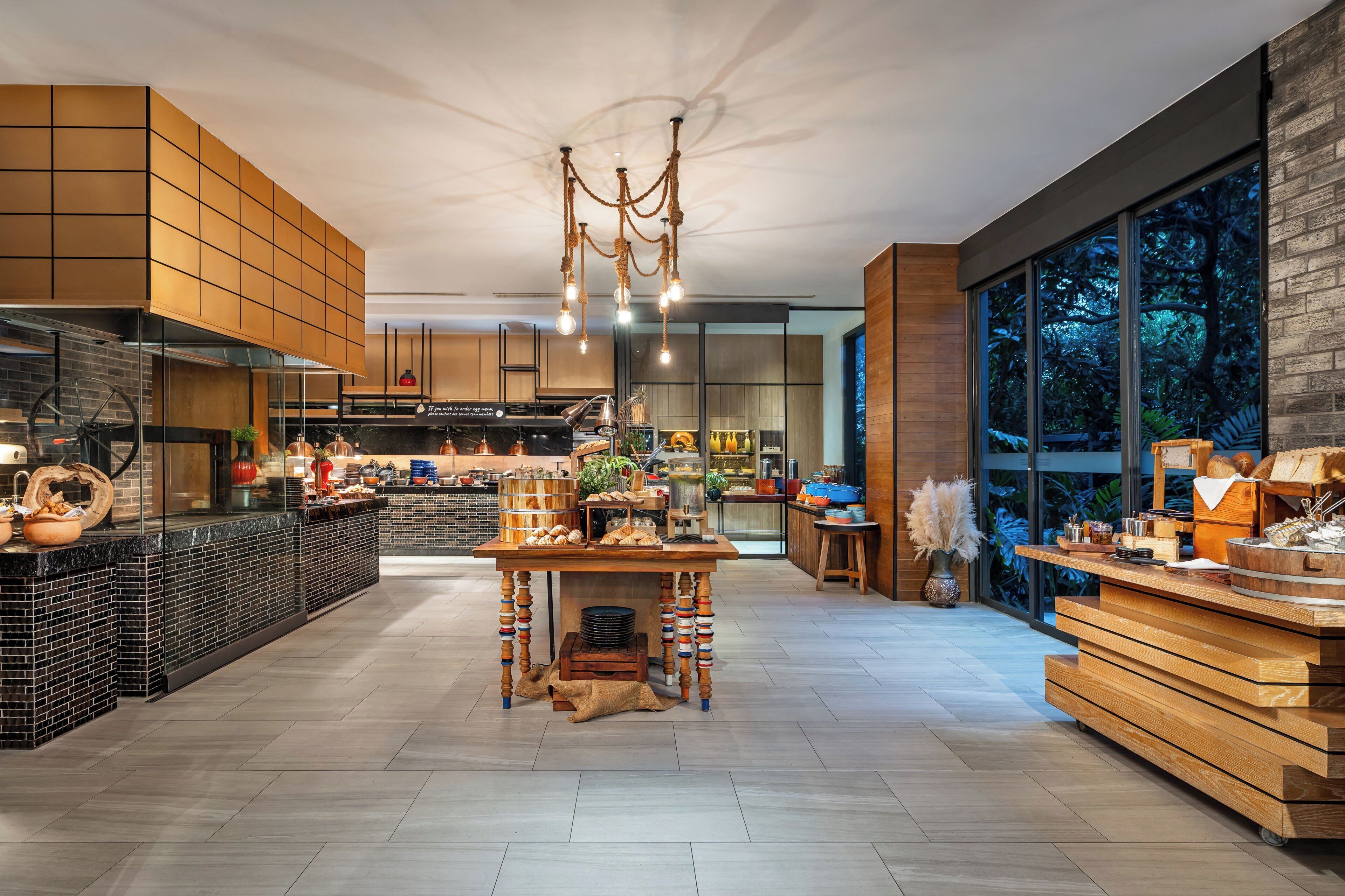 A modern kitchen with a central island, a dining area, and large windows offering a view of the outdoors.