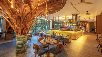 A modern restaurant with a central dining area, a bar, and a kitchen visible through large windows.
