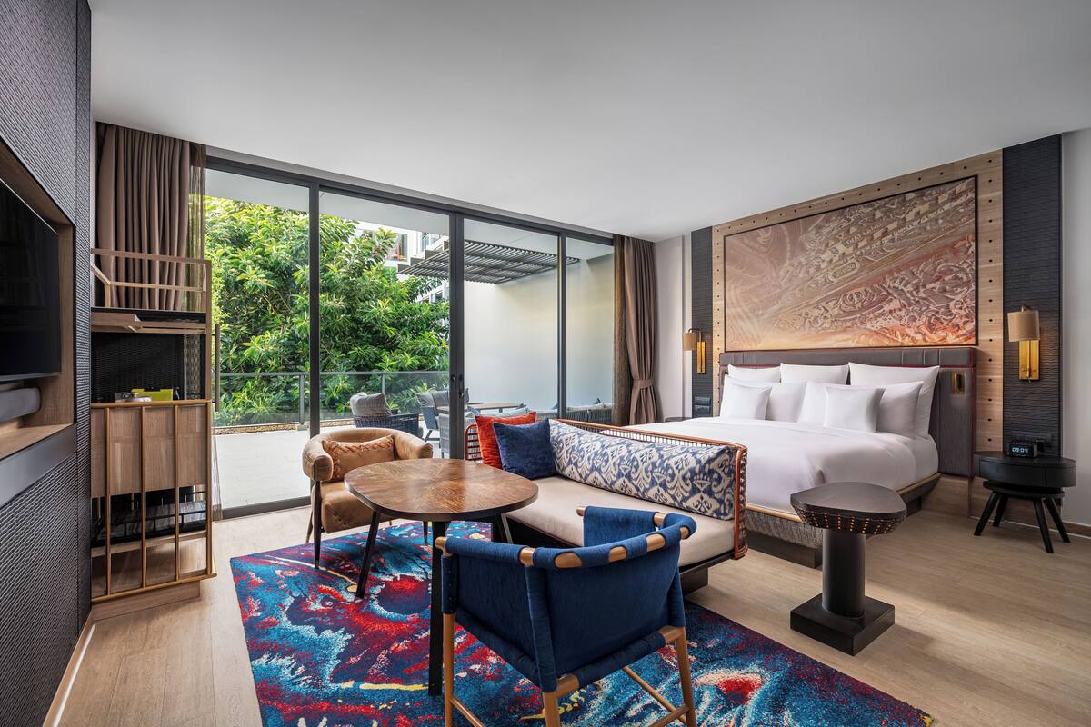 A modern hotel room with a large bed, a sofa, a dining table, and a TV.