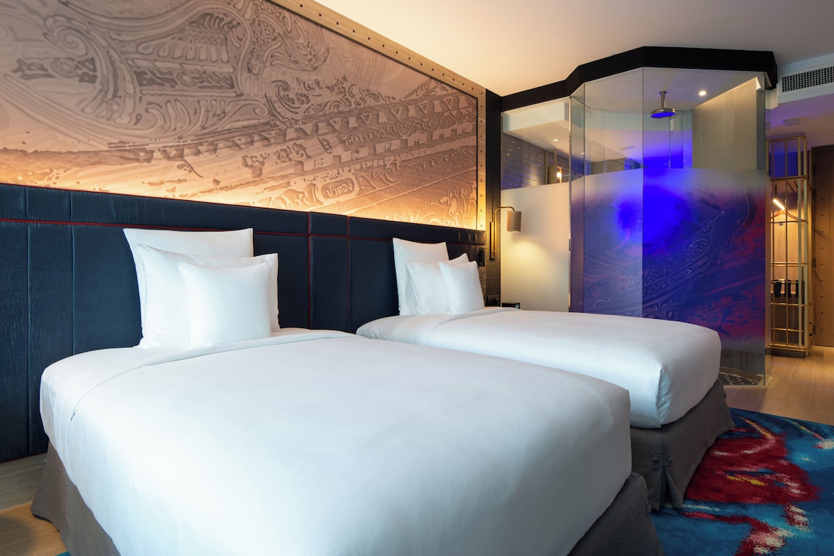 Habitación de hotel con dos camas, un gran muro decorativo y una pared de vidrio.