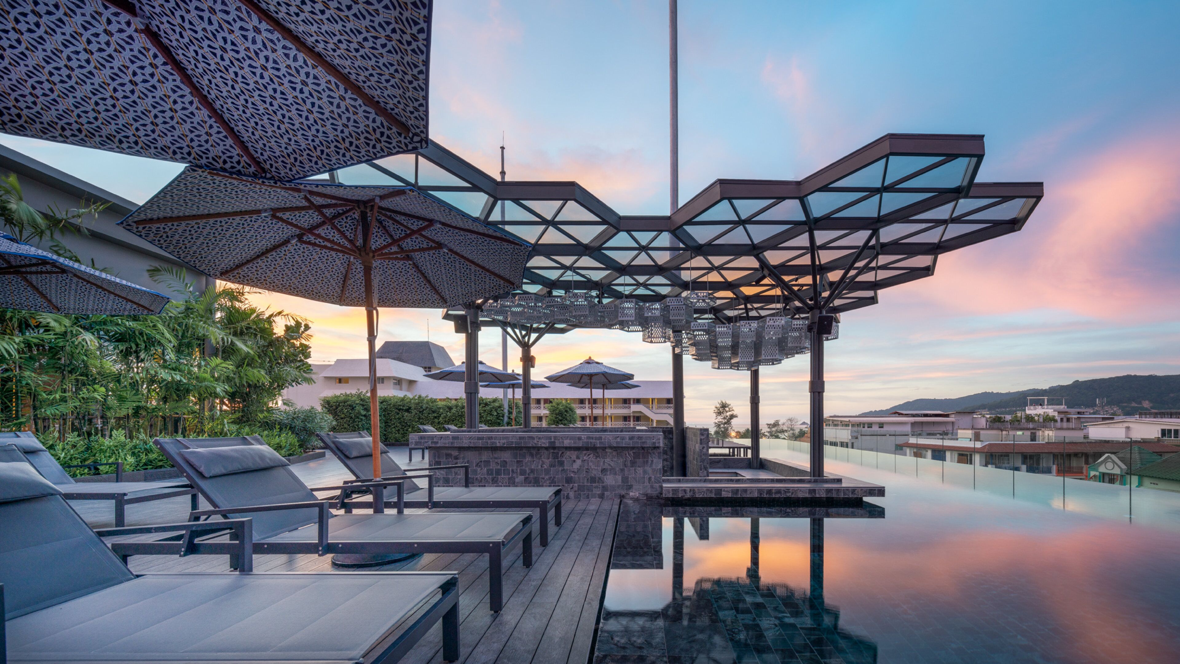 Ein Fernblick auf eine Stadtlandschaft, umgeben von Grün, mit einem Infinity-Pool, Liegestühlen und Sonnenschirmen.