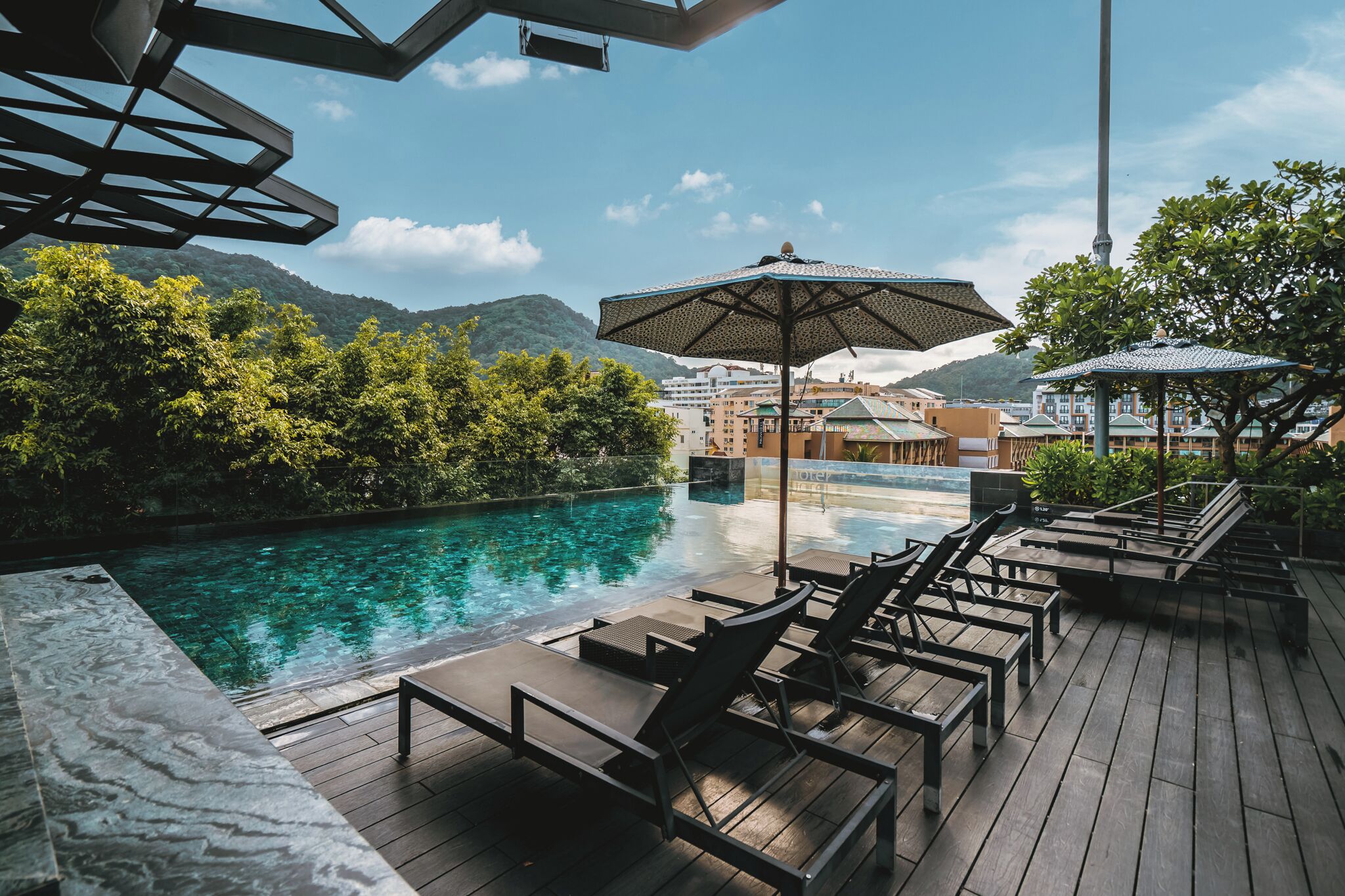 A poolside area with lounge chairs and umbrellas, overlooking a pool and lush greenery.