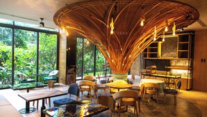 Een modern interieur met een groot, gebogen bamboeplafond, een eethoek met ronde tafels en stoelen, en grote ramen met uitzicht op weelderig groen.