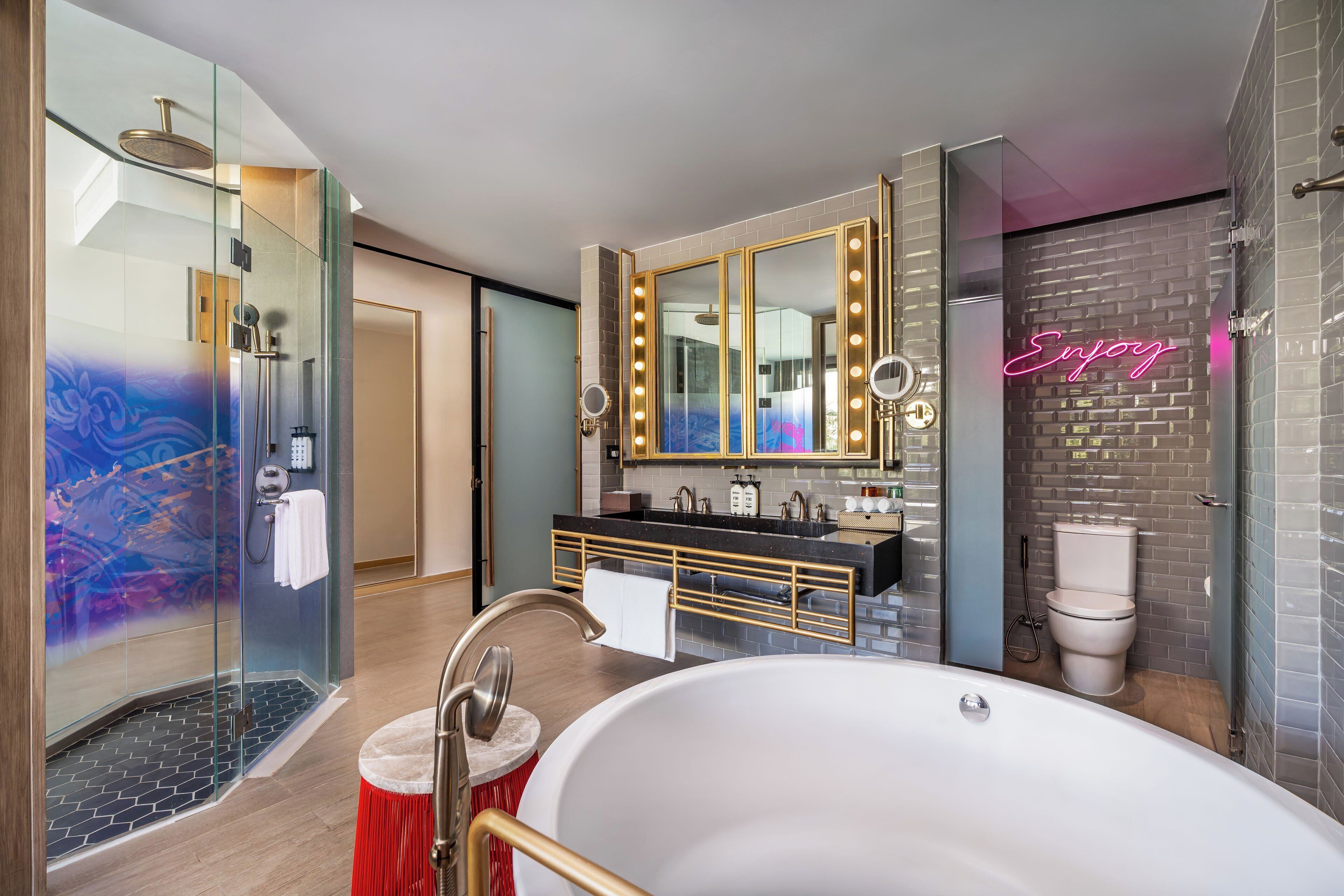 A modern bathroom with a glass-enclosed shower, a freestanding bathtub, a vanity with a large mirror and lights, and a neon sign.