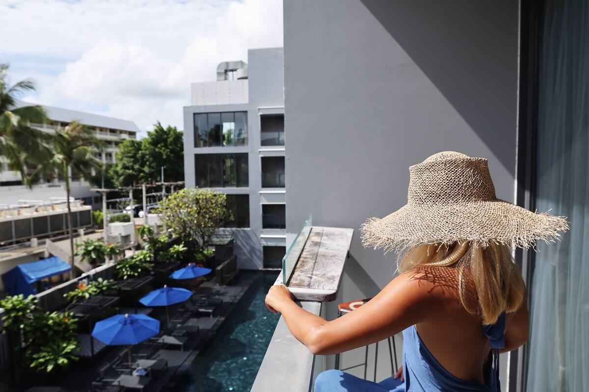 A person sitting by a pool with lounge chairs and umbrellas, overlooking a modern building and a clear sky.