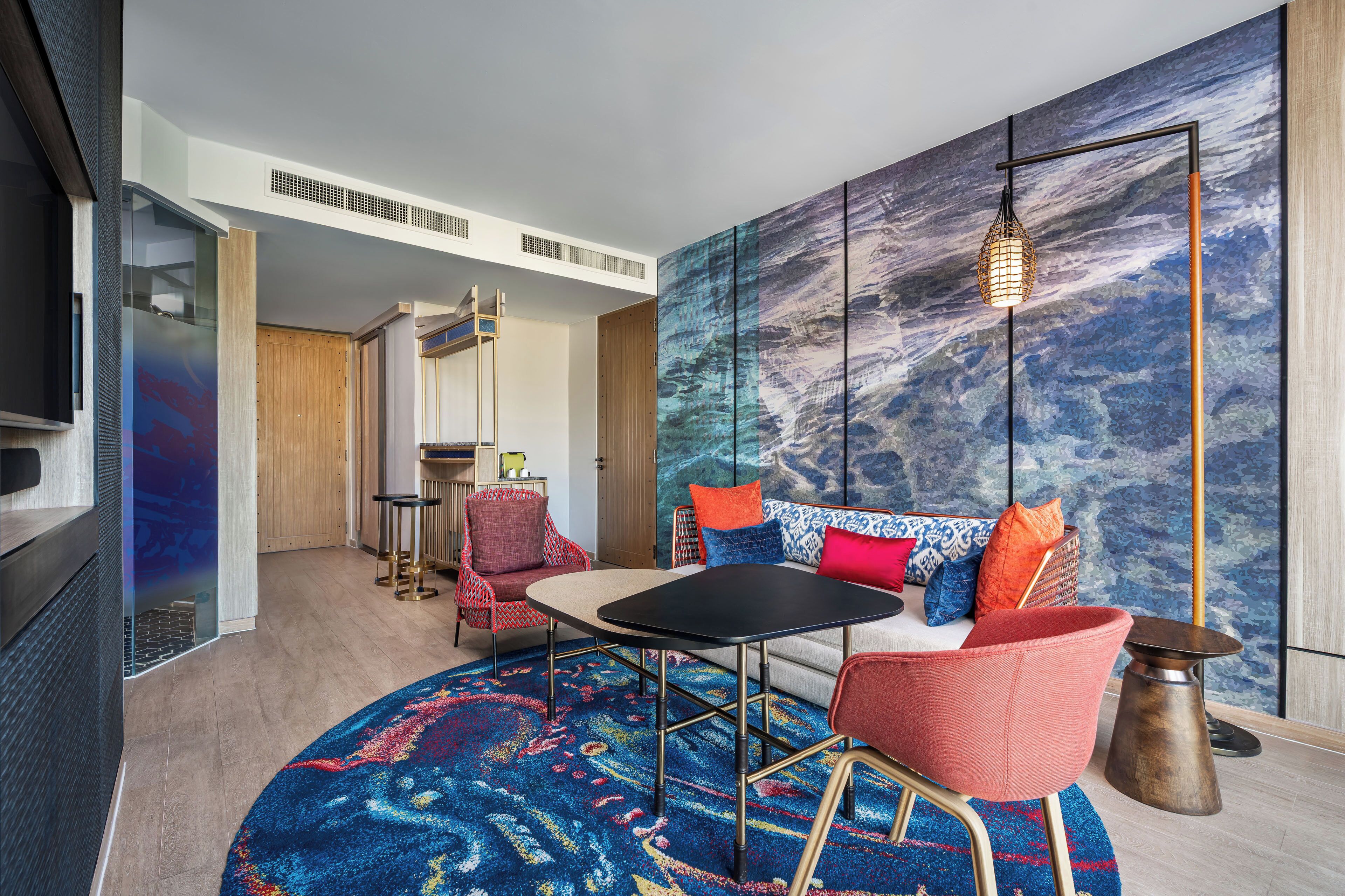 Un salon moderne avec un canapé, des fauteuils, une table basse et une grande fresque abstraite sur le mur.