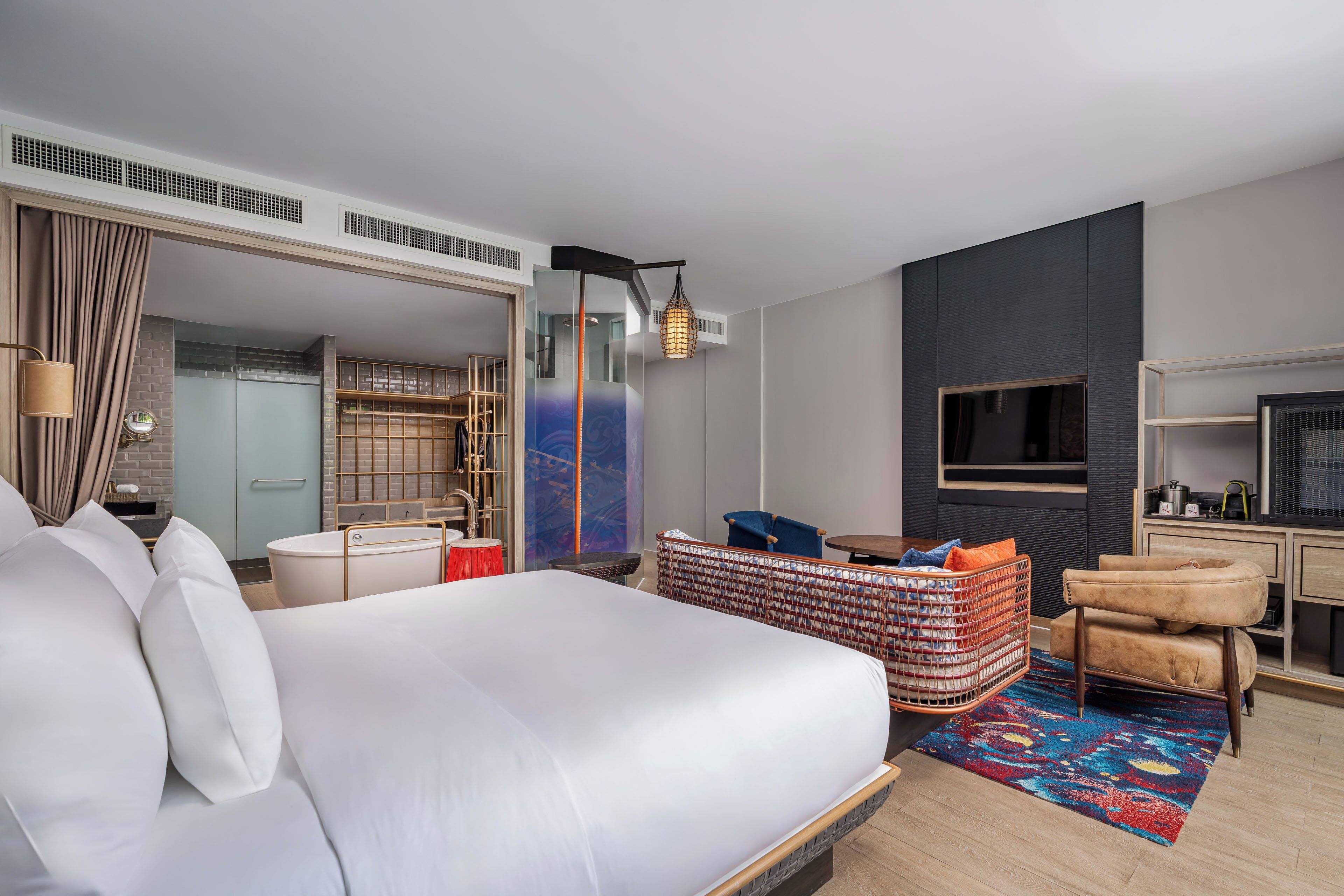 Una habitación de hotel moderna con una cama grande, una zona de estar con un taburete estampado, un televisor y una kitchenette.