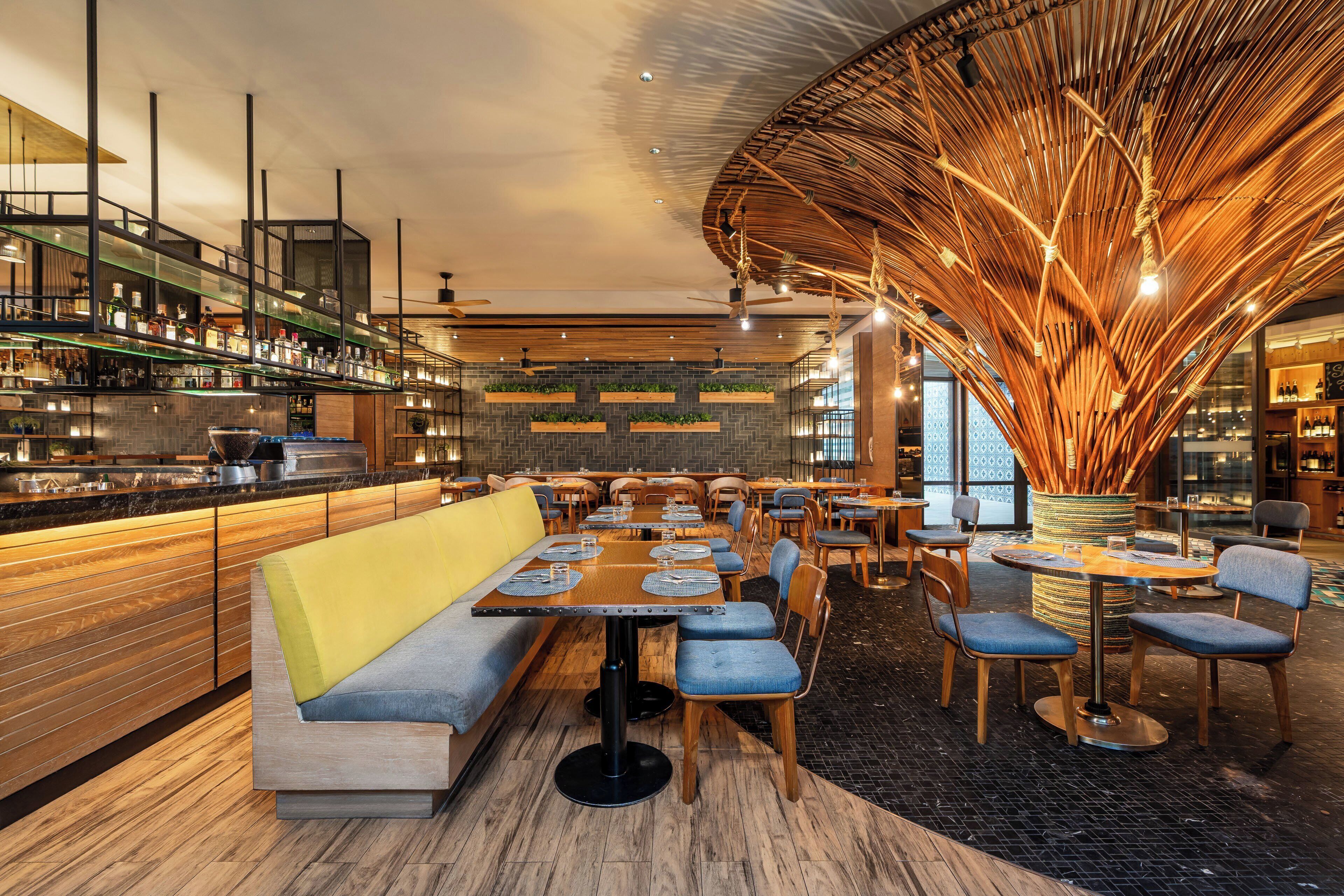En modern restaurang med ett centralt placerat sittområde, en bar med hyllor fulla av flaskor och en unik takdesign.