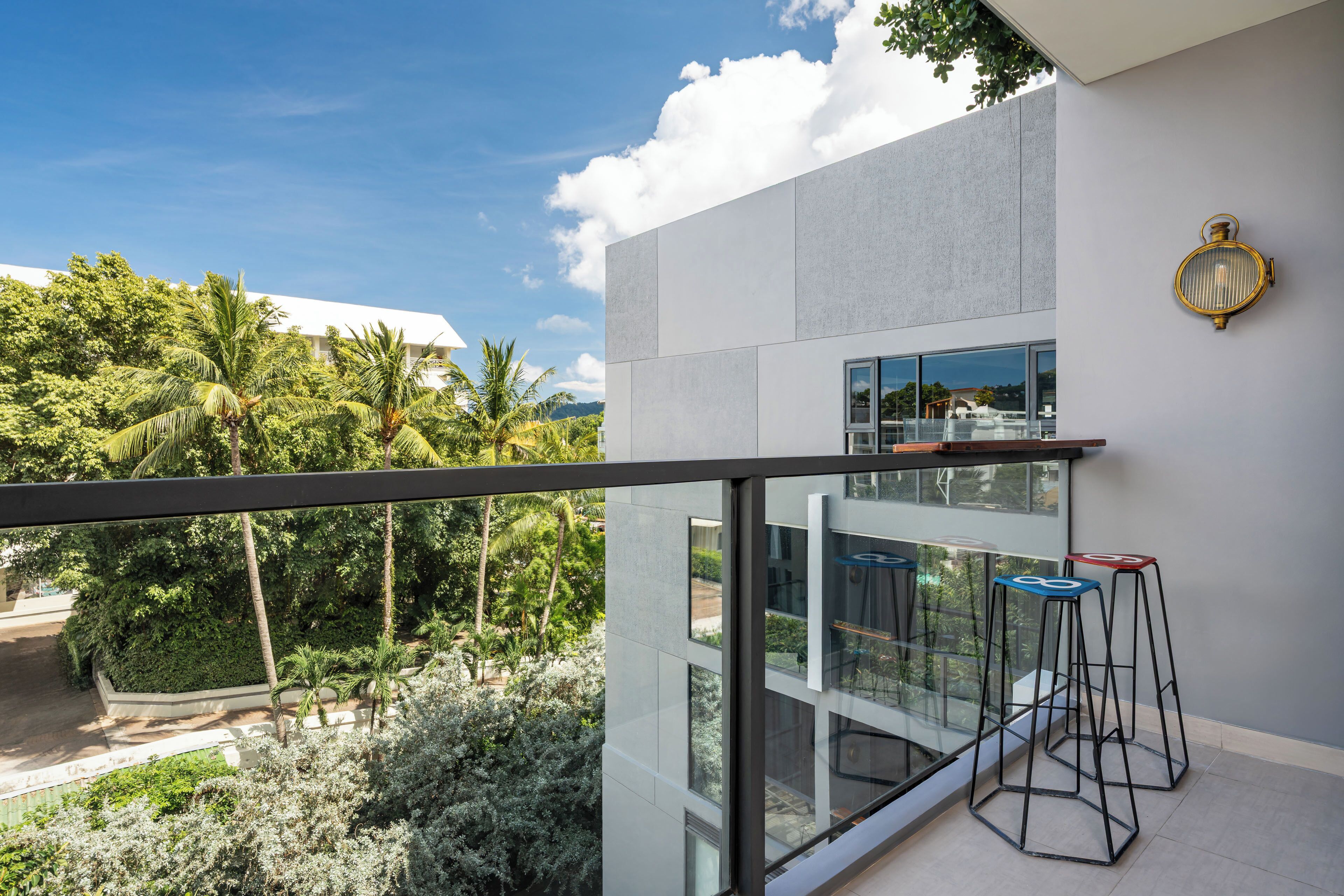 Un bâtiment moderne doté d’un balcon donnant sur un jardin luxuriant et des palmiers.