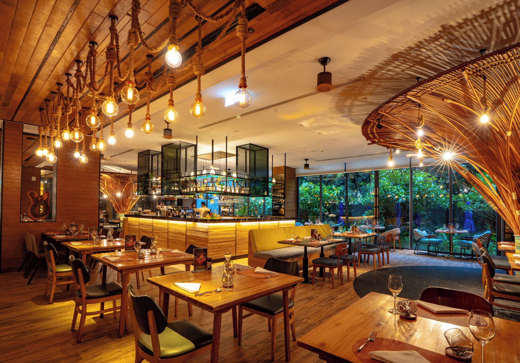Un restaurant avec des tables et des chaises en bois, un coin bar et de grandes fenêtres donnant sur un paysage verdoyant.
