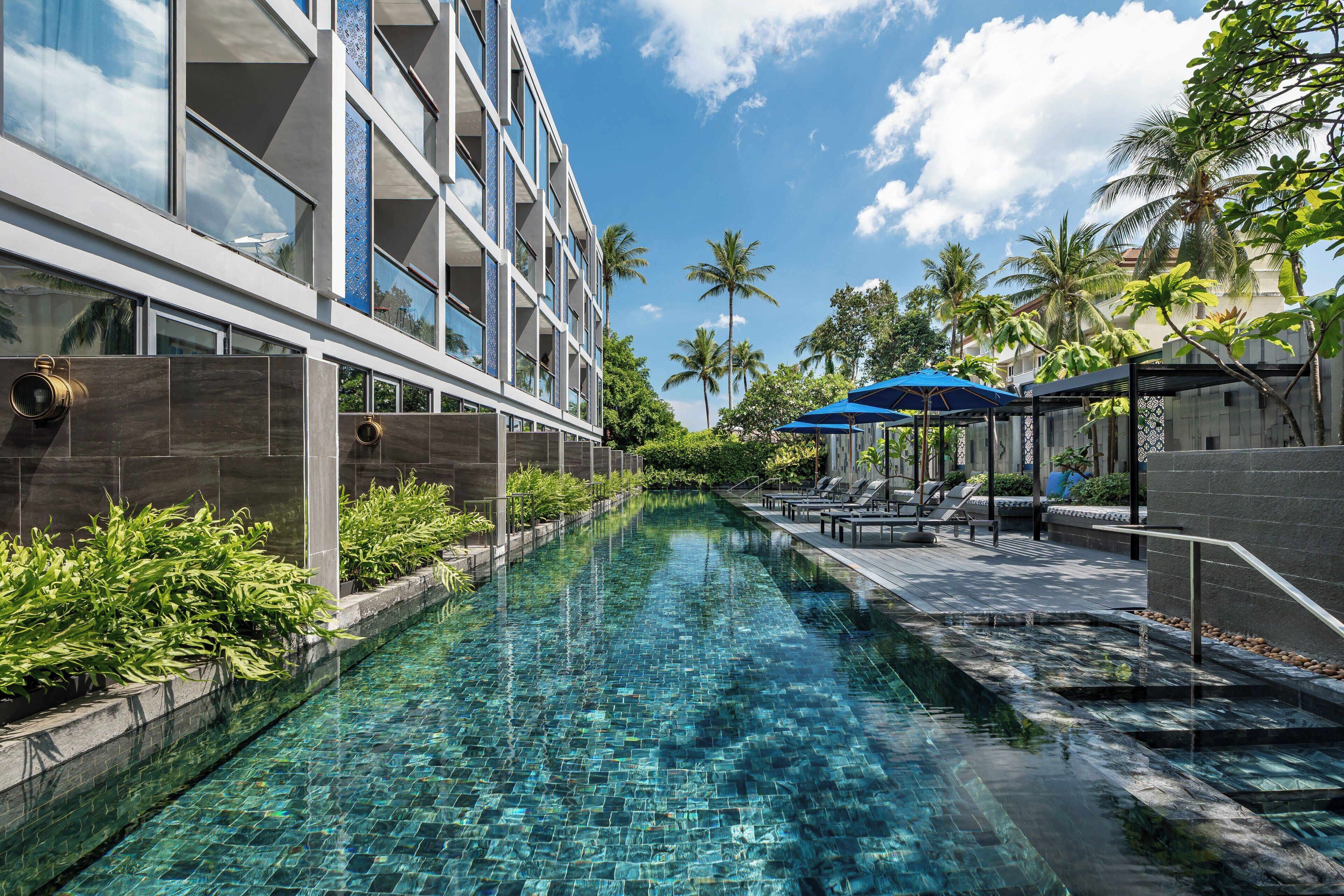 A modern hotel with a swimming pool, palm trees, and lounge chairs.