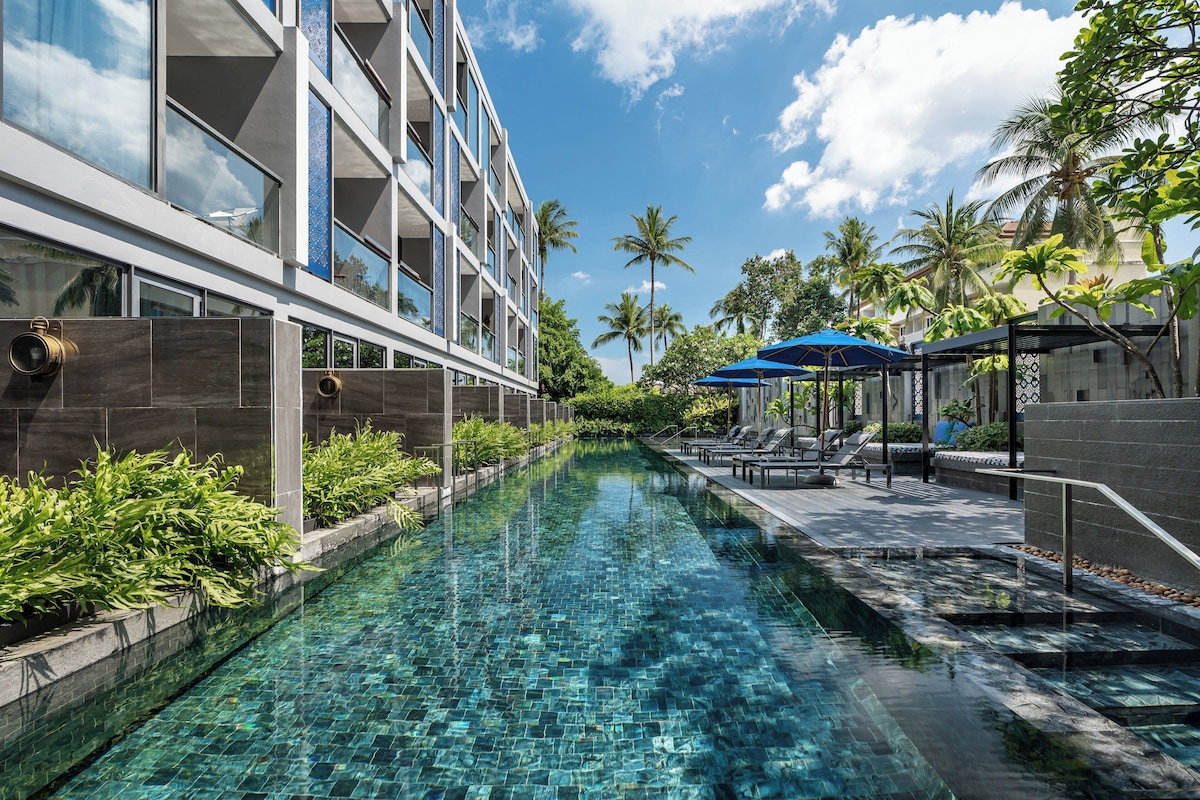 Un hotel moderno con piscina, palmeras y sillones de descanso.