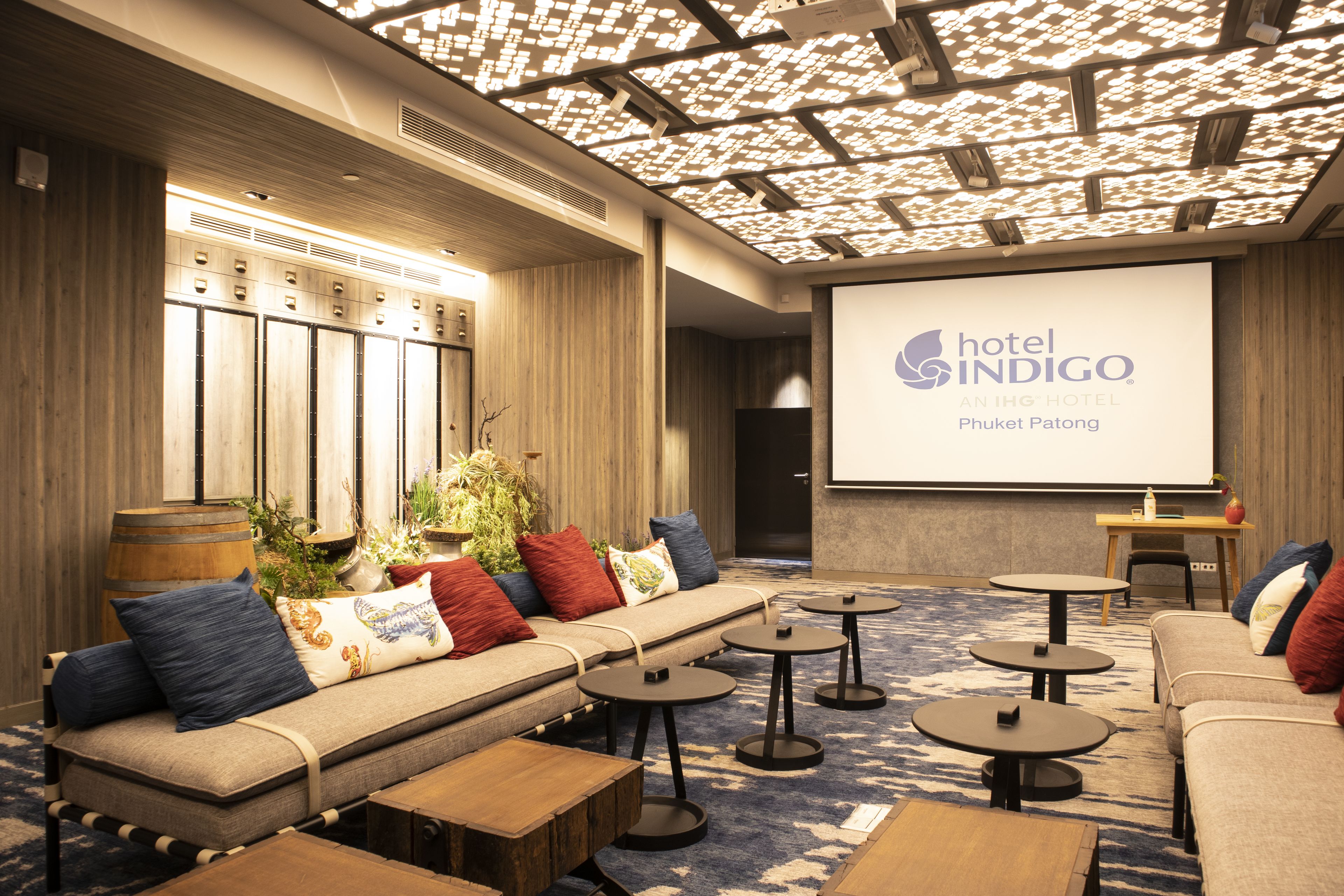 A hotel lobby with seating areas, a projection screen displaying the hotel name, and lockers.