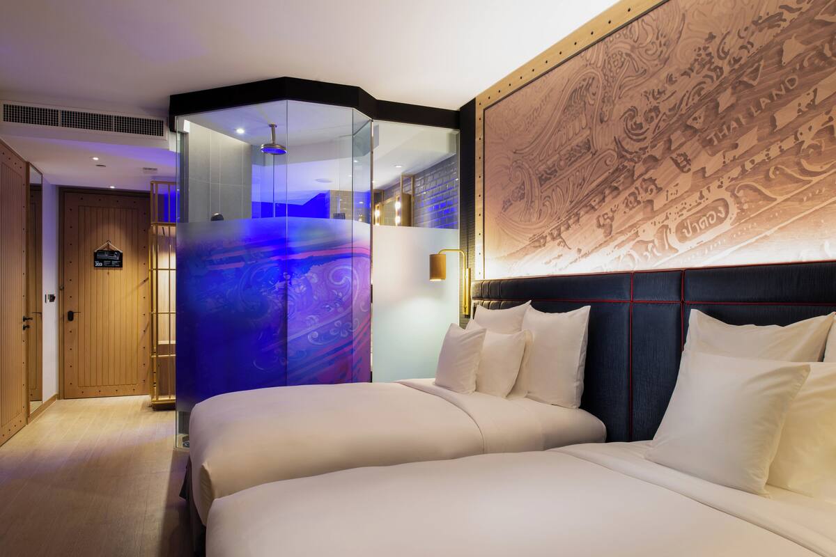 A modern hotel room with a large bed, a glass partition, and a decorative wall mural.