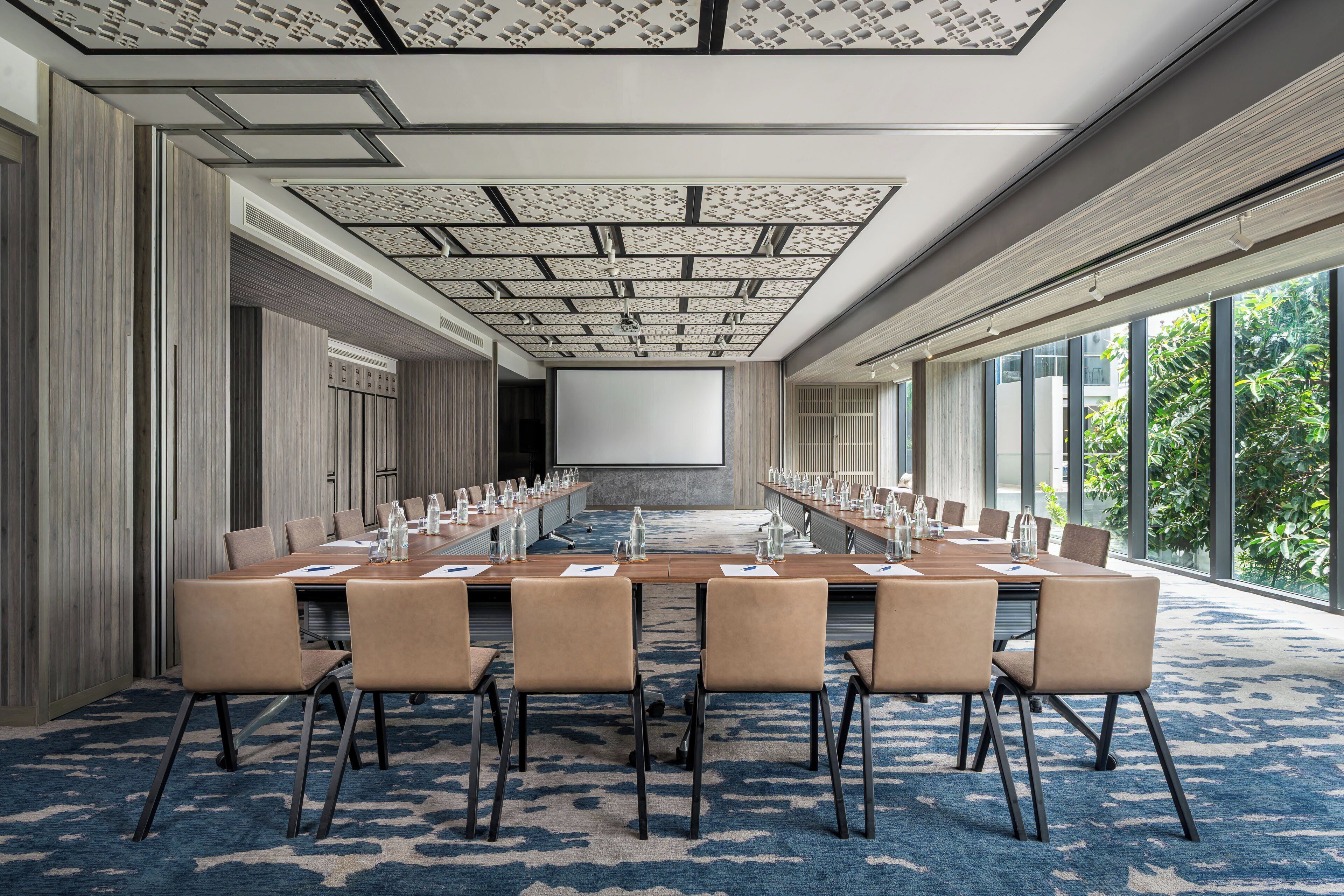 Un salón de conferencias con una larga mesa, sillas y una pantalla para proyector.
