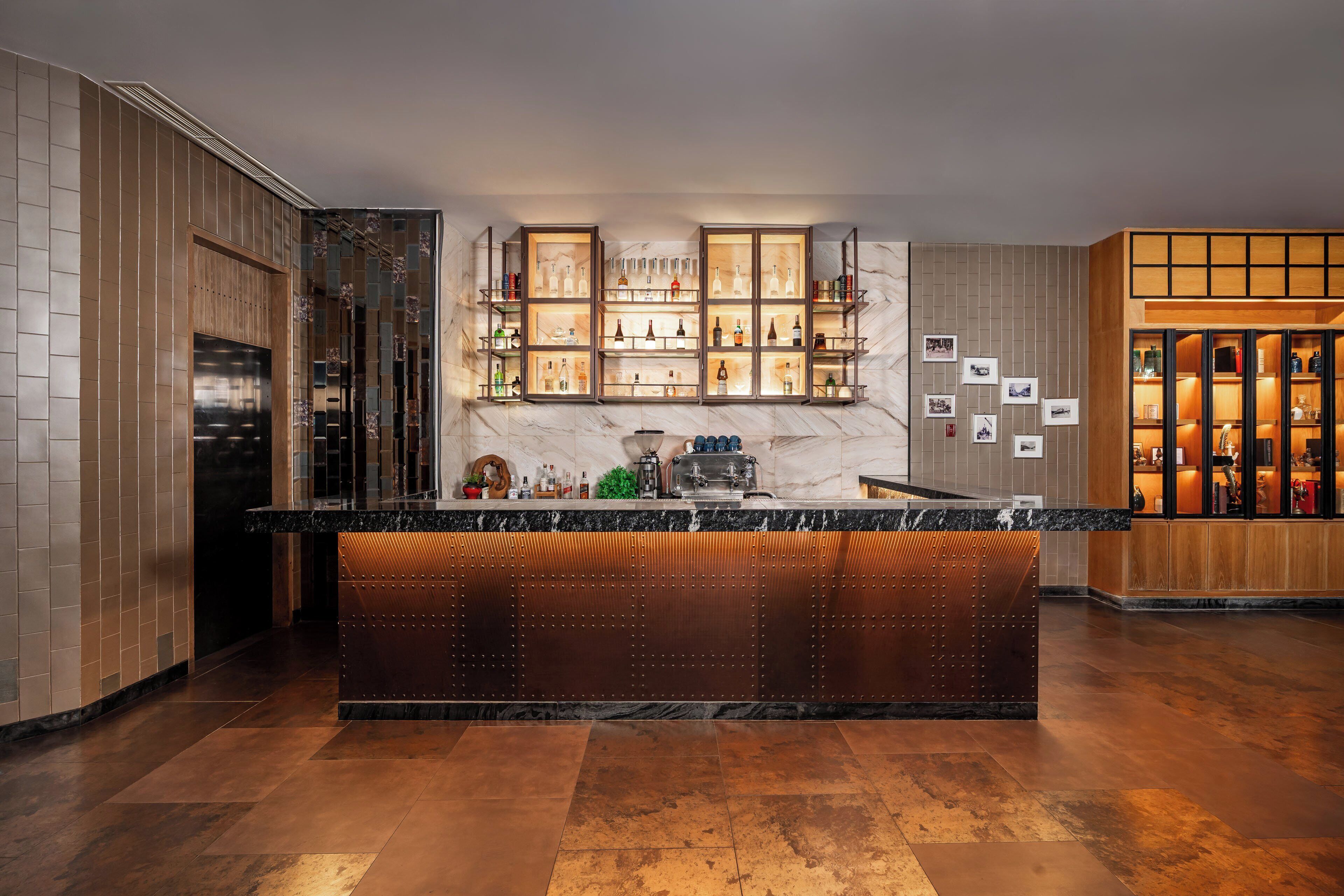 A modern bar area with a marble countertop, multiple shelves of bottles, and a wooden panel wall.
