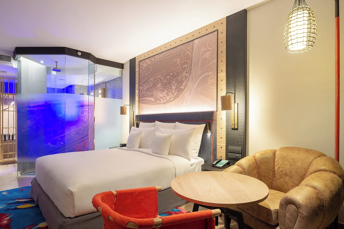 A hotel room with a large bed, a seating area with a table, and a decorative wall piece.