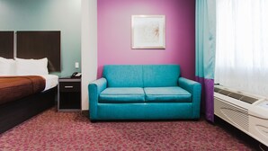 Una habitación de hotel con una cama, un sofá color turquesa, una mesita, una mesita de noche, un cuadro en la pared y una ventana con cortinas.