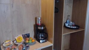 Una kitchenette compacta con cafetera, un cesto de basura y una pequeña mesa con aperitivos y frutas.
