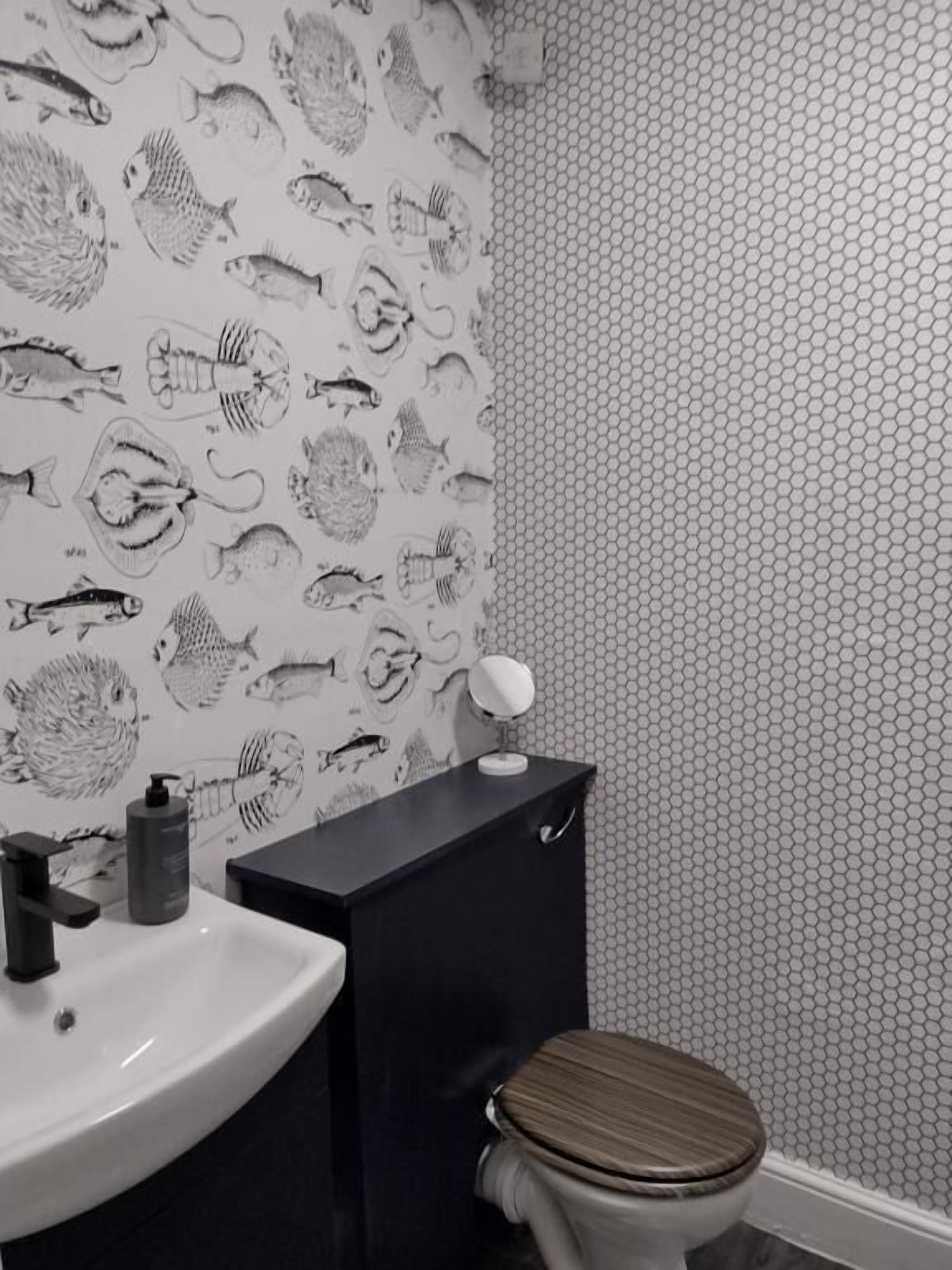 Un baño con lavabo, inodoro y espejo. La pared presenta un diseño con ilustraciones de peces.