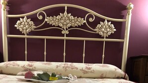 A bed with a floral headboard, a floral bedspread, and red rose petals scattered on the bed. - Hostal Hostatgeria Sant Jaume (La Pobla de Benifassa)