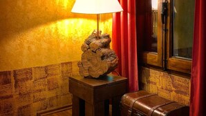 A room with a wooden bench, a lamp on a small table, and a red curtain. - Hostal Hostatgeria Sant Jaume (La Pobla de Benifassa)
