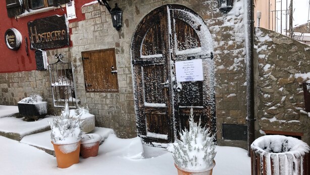 A snow-covered building with a rustic wooden door, potted plants, and a stone wall. - Hostal Hostatgeria Sant Jaume (La Pobla de Benifassa)