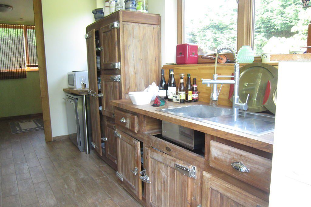 A kitchen with wooden cabinets, a stainless steel sink, and various bottles on the counter.