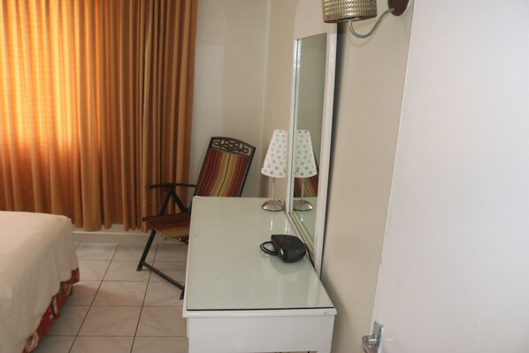A hotel room with a bed, a desk with a lamp, a chair, and a large mirror.