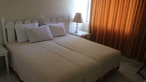 A neatly made bed with a white headboard, a bedside table with a lamp, and a window with curtains.