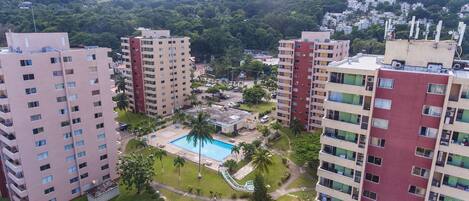 Un edificio residencial de gran altura con múltiples balcones, un patio central con piscina y zonas verdes circundantes.