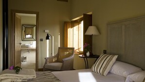 A hotel room with a bed, a chair, a nightstand, a lamp, and a view of the bathroom. - Hotel Rural Duende del Chafaril (San Martin de Trevejo)