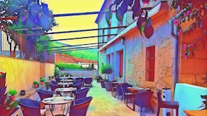 An outdoor café area with round tables and chairs, potted plants, and a stone floor. - Hotel Rural Duende del Chafaril (San Martin de Trevejo)