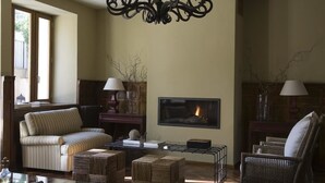A cozy living room with a fireplace, a sofa, a coffee table, and wicker furniture. - Hotel Rural Duende del Chafaril (San Martin de Trevejo)