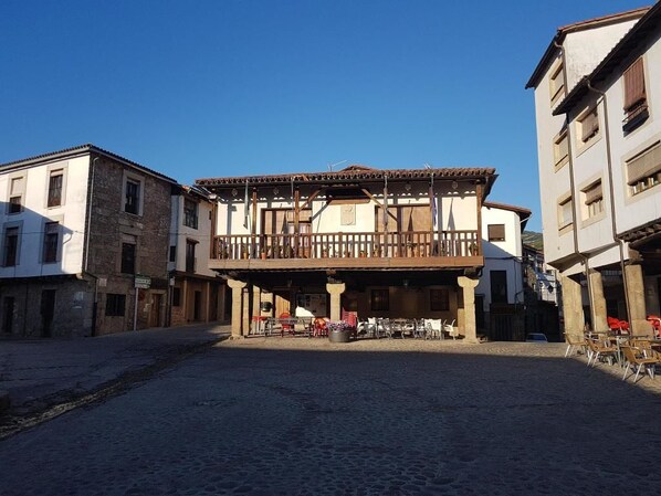 Una calle adoquinada con un edificio que tiene un balcón de madera y mesas al aire libre.