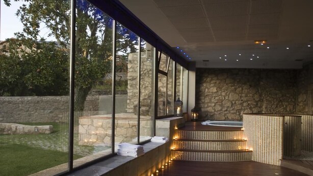 A spa area with a stone wall, wooden deck, and a hot tub. - Hotel Rural Duende del Chafaril (San Martin de Trevejo)
