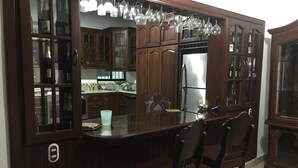 Een keuken met houten kastjes, een eettafel met glazen blad en hangende lampen.