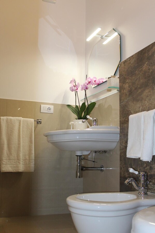 A bathroom with a white sink, a mirror, a towel rack, and a potted orchid.