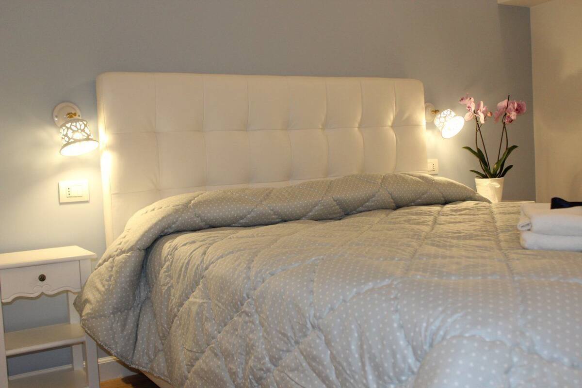 A neatly made bed with a grey polka dot duvet, a white headboard, and two wall-mounted lamps.