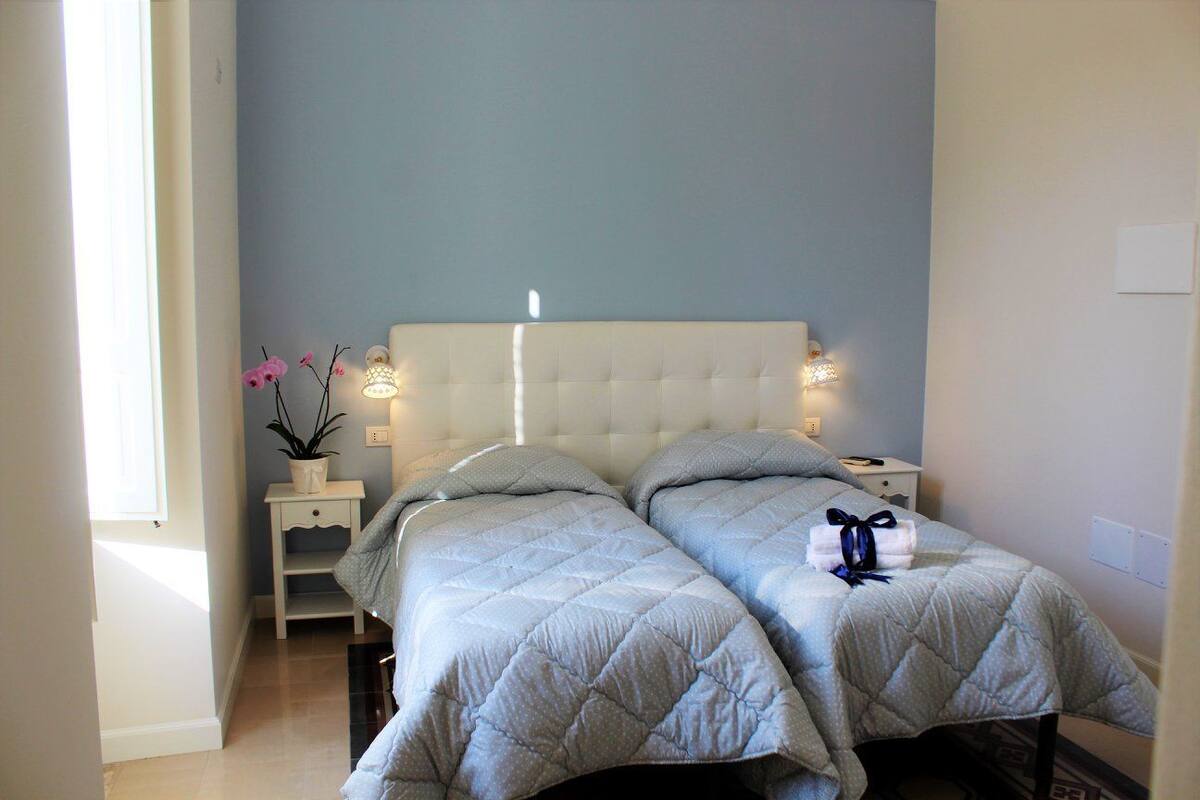A bedroom with two beds, a bedside table with a lamp, and a potted plant.