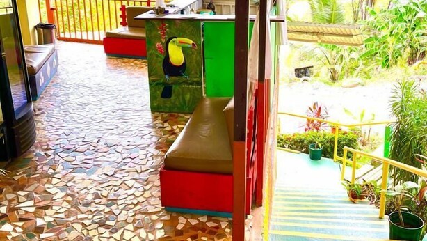 Un'area esterna coperta con pavimento piastrellato, una panchina e un tavolino con un mobiletto verde.