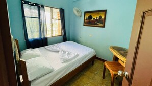 Una stanza con un letto, una scrivania, una finestra con tende, una ventola e un quadro appeso al muro.