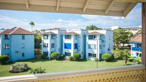 A courtyard with blue buildings, a covered walkway, and green lawns. - Beach Studio  at Point Village Resort (Negril)