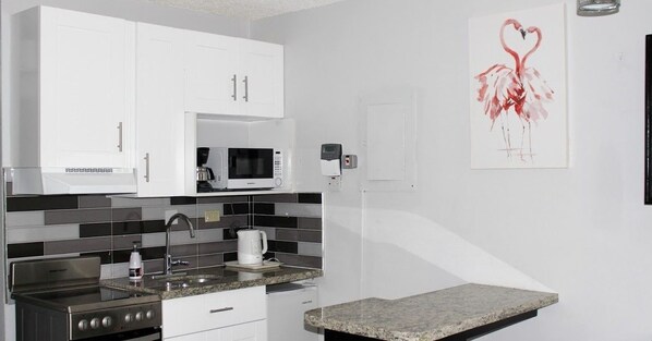 Una cocina moderna con armarios blancos, microondas, cafetera y encimera de granito.