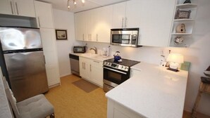 Una cocina compacta con gabinetes blancos, un refrigerador de acero inoxidable, un microondas, una estufa y un lavamanos pequeño.