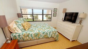Un dormitorio con cama, cómoda, televisor y ventana con vistas al océano.