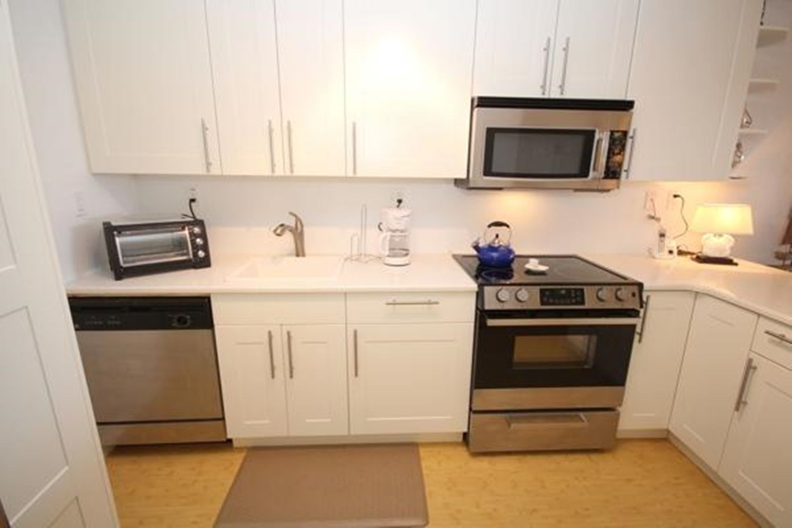 A compact kitchen with white cabinets, a microwave, a toaster, a coffee maker, and a stove.