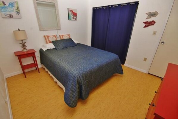 A bedroom with a bed, a nightstand, a lamp, and a door with a sign.