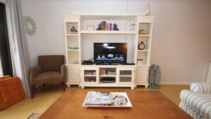 Una sala de estar con un televisor sobre un mueble blanco, un sofá marrón y un sillón a rayas.